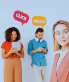 The image shows three people interacting with technology. The first person is a woman wearing a bright orange top and lighter orange pants, holding a tablet in both hands. To her left is a man in a light blue shirt and antique white pants, with white headphones around his neck and a cellphone in his hand. The third person, another woman, is wearing a light orange jacket over a white blouse. She holds a cellphone in her left hand, raising it as if taking a selfie. Above the first woman and the man, the words "Share," "Click," and "Hello" appear, representing social media activity.