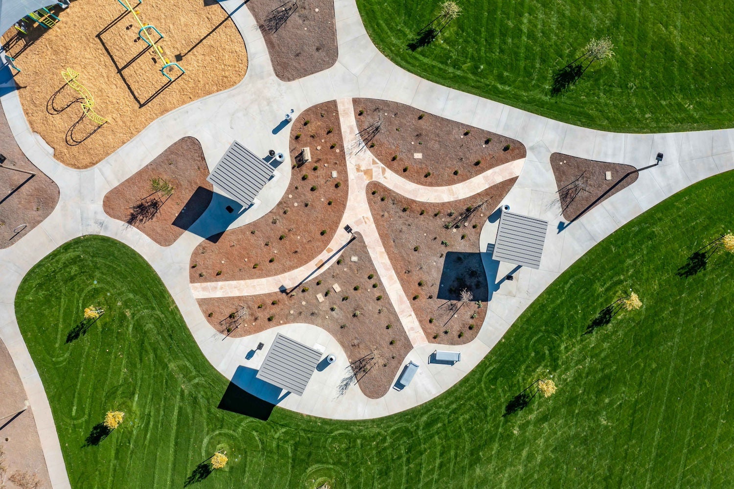 Aerial photograph of a city park, with ramadas, bennches, and other playground equipment surrounded by sidewalks and grass.