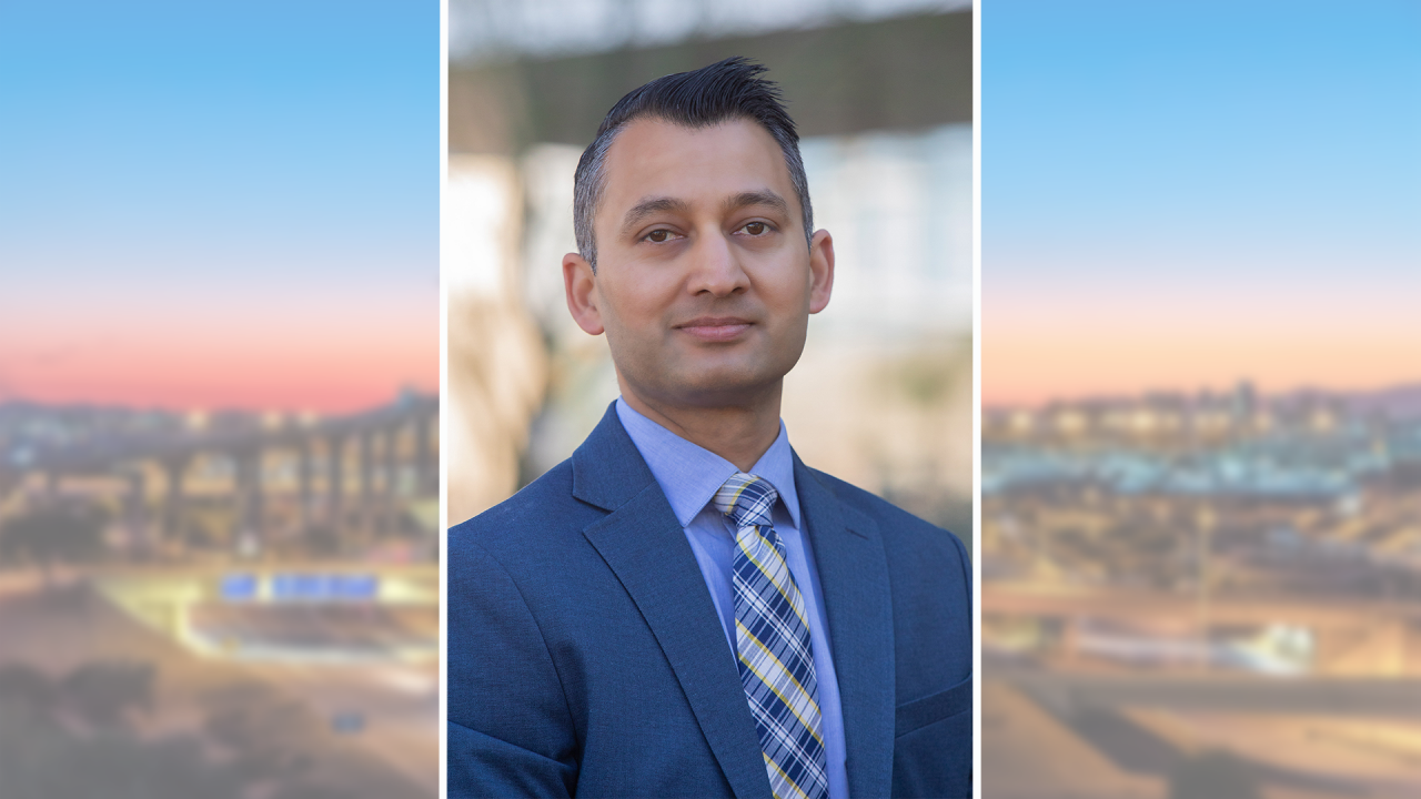 Daver Malik headshot image in blue business suit and tie in front of building. Photo is overlayed on top of a faint Phoenix Sky Harbor evening sunset photo on both sides.